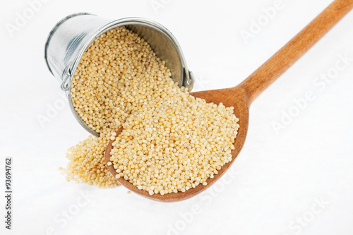 Bucket of millet crumbles in the a wooden spoon
