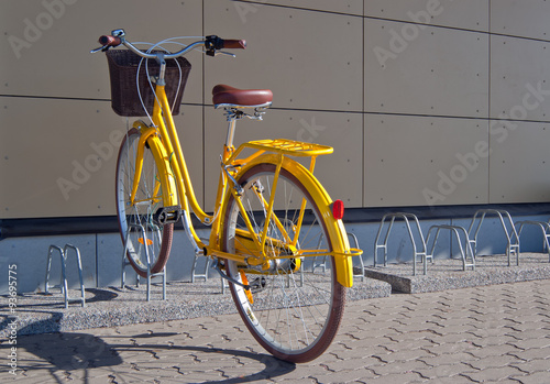 Yellow bike with basket parking at bike rack on street.