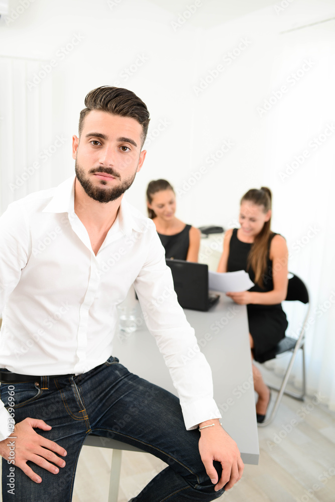 portrait of a handsome young business man in casual wear standing in office with working partner in background portrait of a handsome young business man in casual wear standing in office with working partner in background