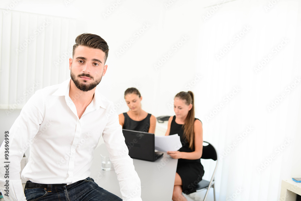 portrait of a handsome young business man in casual wear standing in office with working partner in background portrait of a handsome young business man in casual wear standing in office with working partner in background