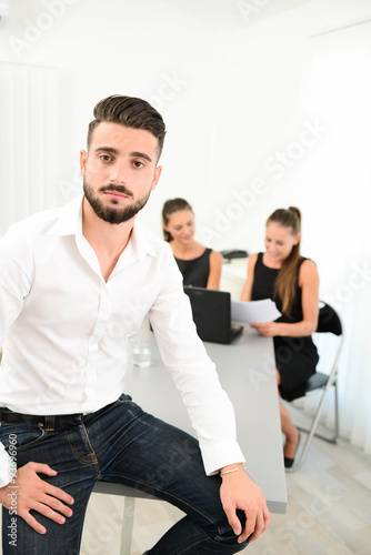portrait of a handsome young business man in casual wear standing in office with working partner in background