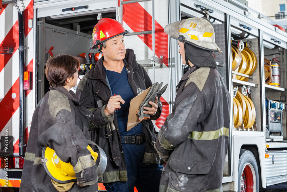 Obraz premium Firefighters Discussing Against Truck At Fire Station