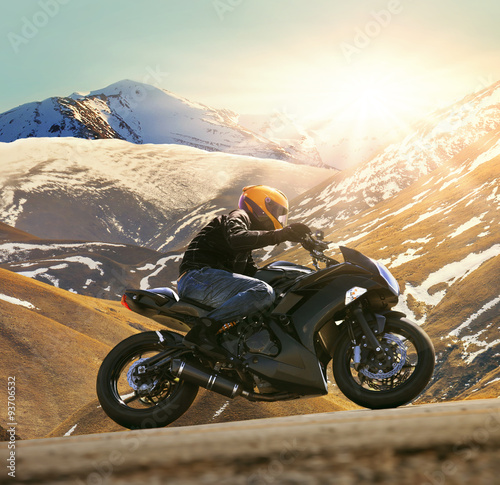 Fotografie young man riding motorcycle on asphalt country road with sun shi