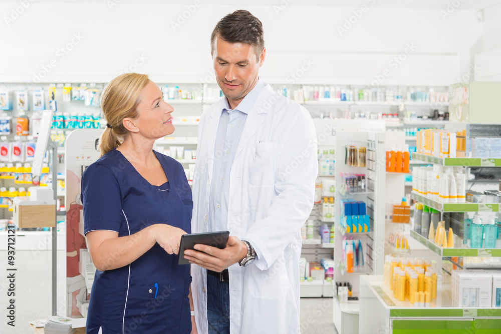 Assistant Looking At Pharmacist Using Digital Tablet