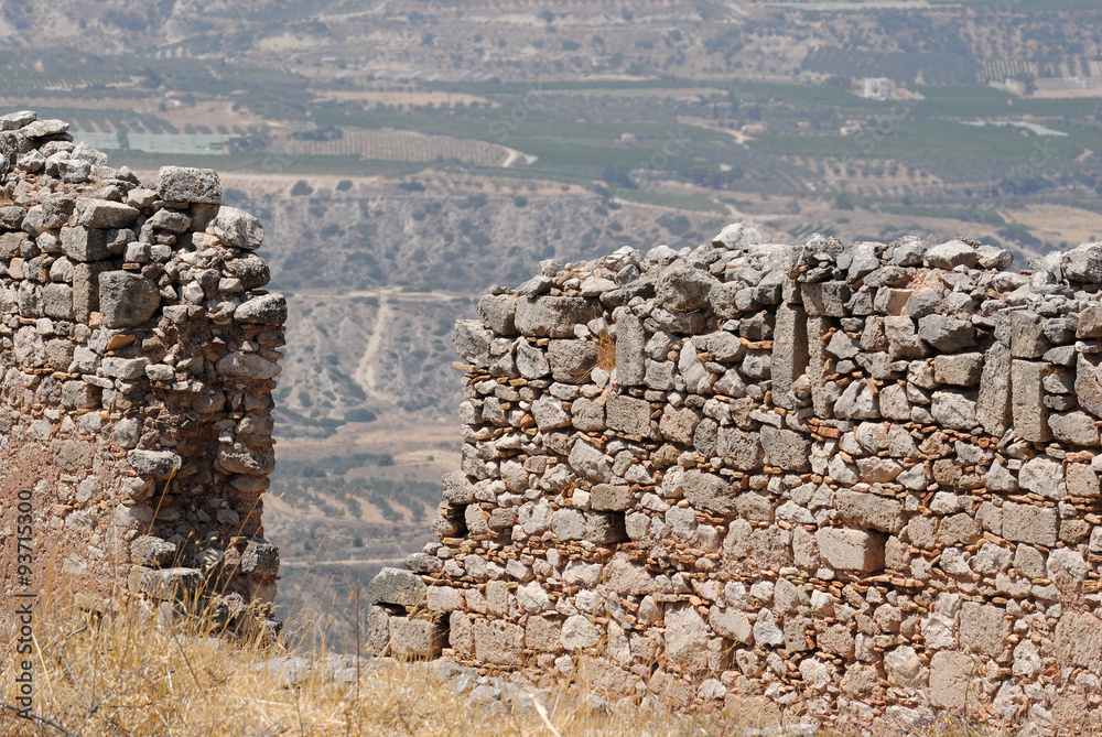 Ruins of stone fortress wall of the ancient city of Corinth with views of the mountain valley on a bright sunny day.