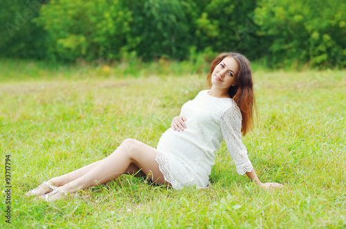 Beautiful young pregnant woman lying on grass summer