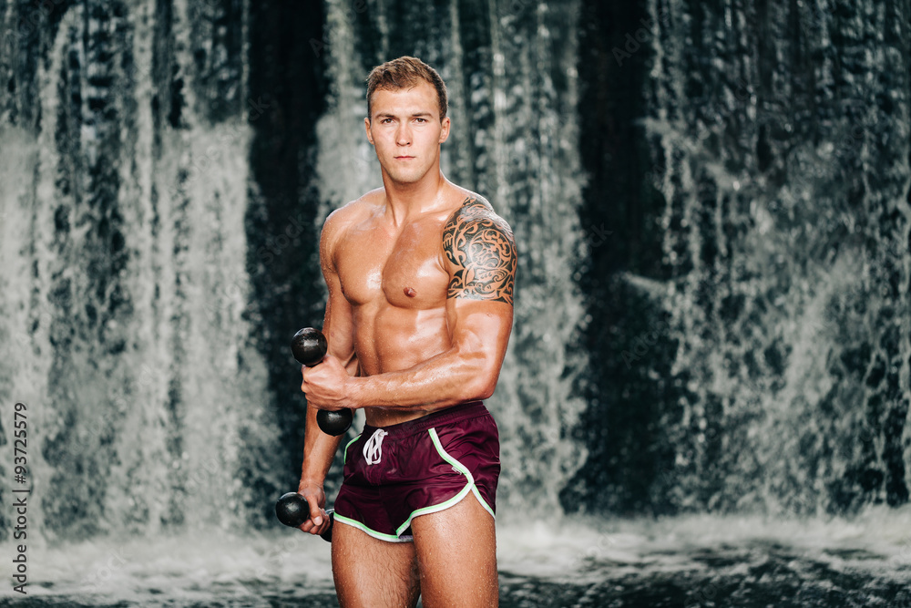 Muscular man lifting dumbbell on waterfall Muscular man lifting dumbbell on waterfall
