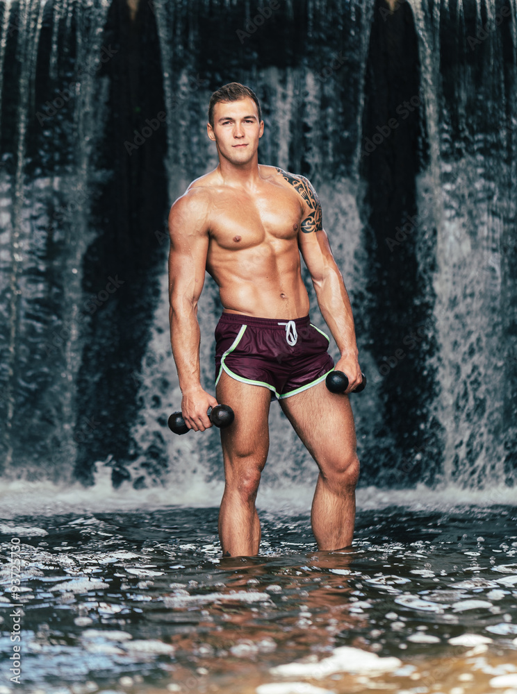 Muscular man lifting dumbbell on waterfall Muscular man lifting dumbbell on waterfall