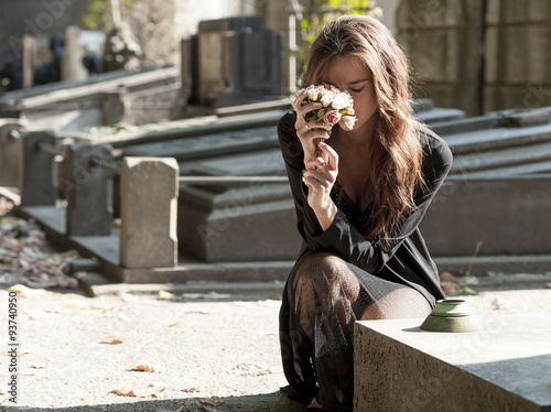 Fotografia Sad woman holding bunch of flowers near a grave