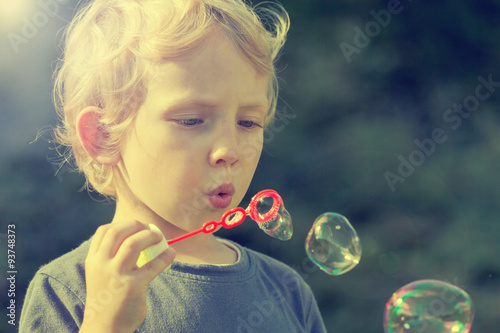 Little blond boy with soapy bubbles outdoors