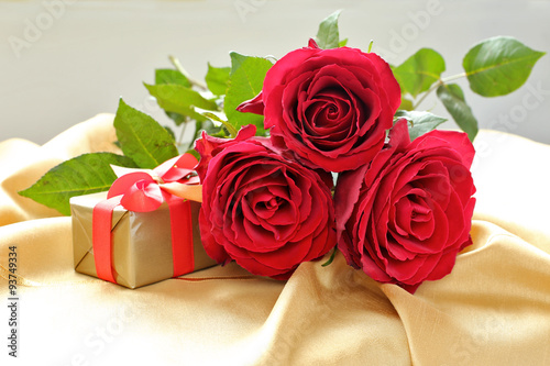 Roses with gift box on gold tablecloth.
