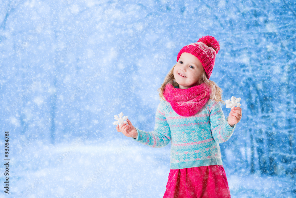 Little girl playing with toy snow flakes in winter park