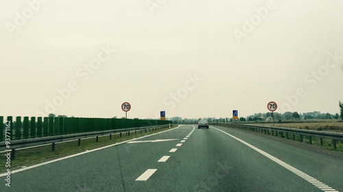 Droga ekspresowa, kończący się lewy pas na drodze, biała strzałka na jezdni i znaki ograniczające prędkość na końcu pasa ulicy	 photo