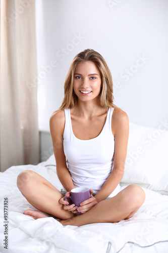 Beautiful woman drinking a coffee sitting on her bed at home