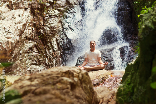 sporty young man practicing yoga near a waterfall in the mountai