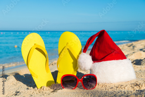 Christmas vacation at sea. Happy New Year holidays. Santa hat, sandals, sunglasses on sandy beach
