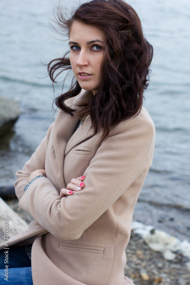 stylish girl in autumn coat sitting by the water