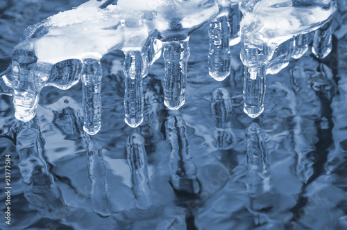 Ice transparent icicles on the river with reflection