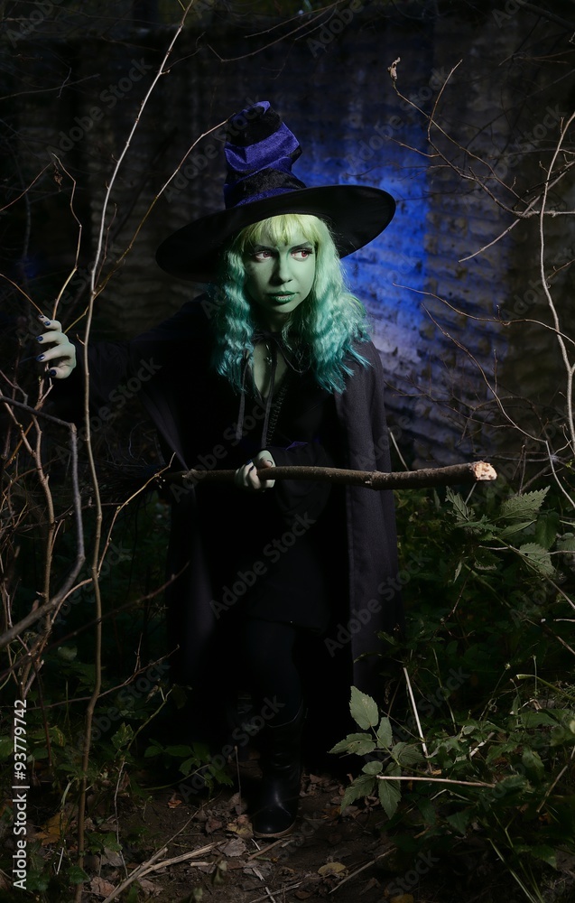 Naklejka premium Young girl with green hair and broom in suit of witch in forest. Halloween time