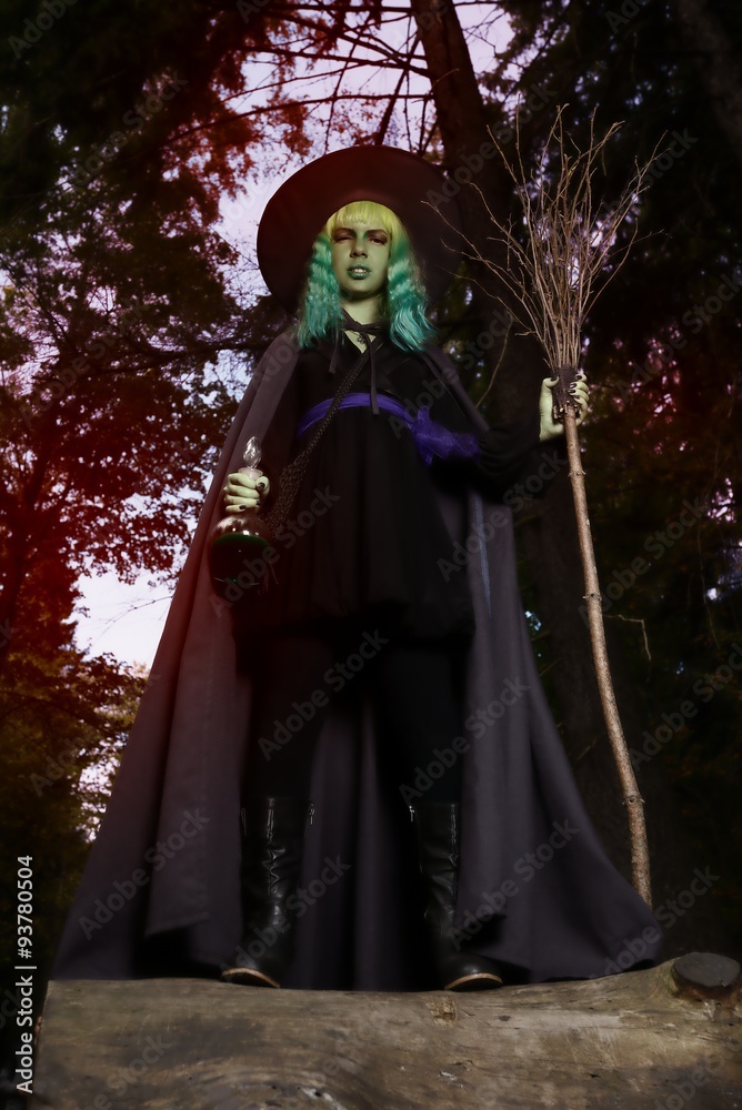 Young girl with green hair and broom in suit of witch in forest. Halloween time