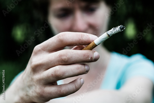 A woman is sitting in a very depressed mood, in the hand between the fingers lit cigarette. 