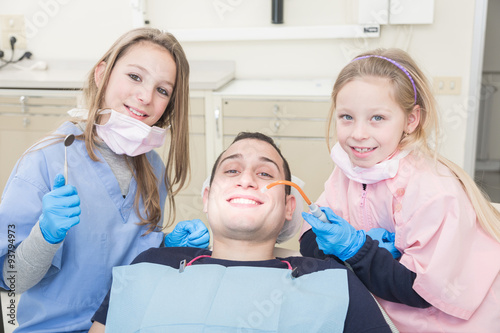 Little dentists examining the mouth of an adult patient photo