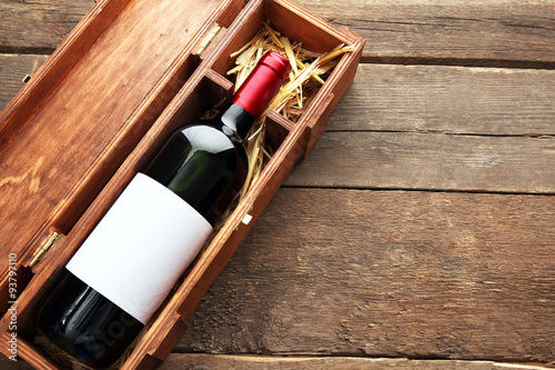 Expensive wine in elegant case with straw on wooden background