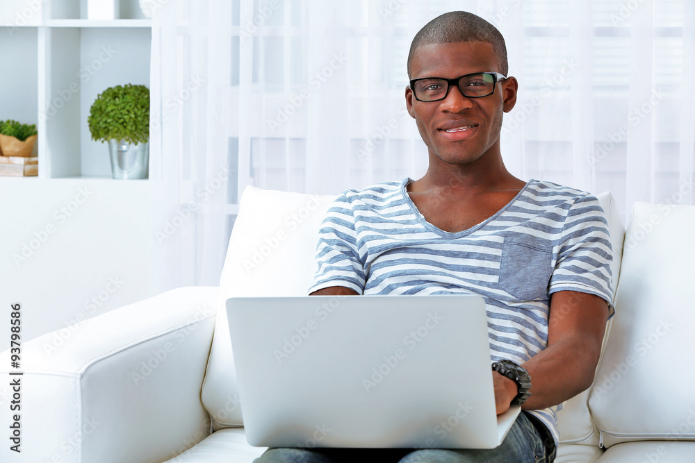 Handsome African American man sitting with laptop on sofa in room Handsome African American man sitting with laptop on sofa in room