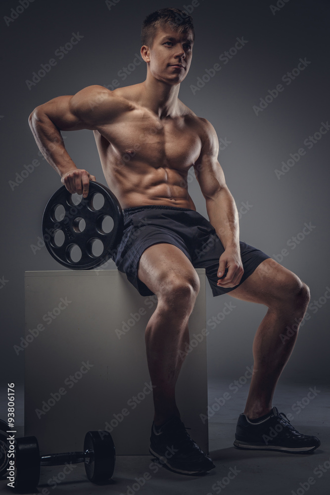 Young bodybuilder sitting on wooden box.