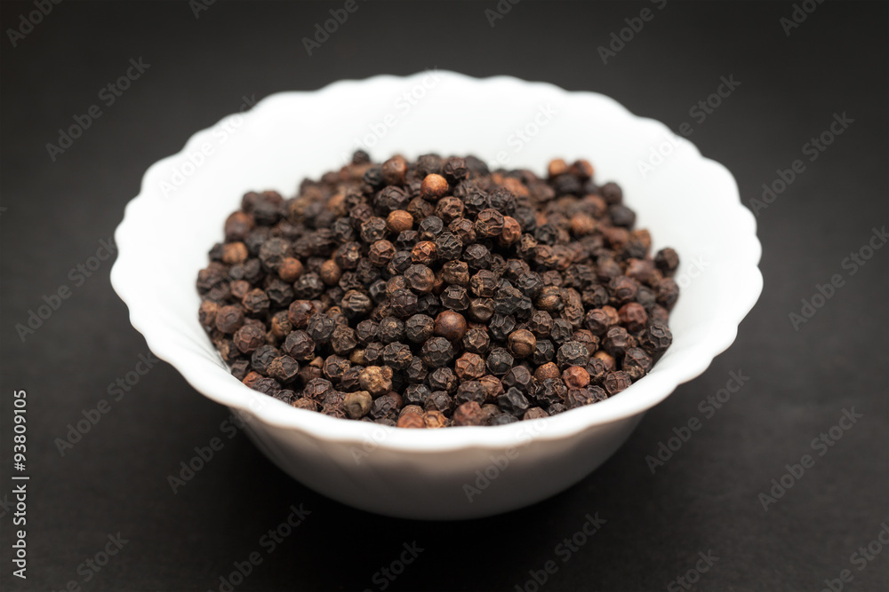 Organic Black pepper (Piper nigrum) in white ceramic bowl on dark background. Organic Black pepper (Piper nigrum) in white ceramic bowl on dark background.
