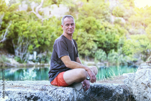A man hiker relaxing sitting on the stone, smiling looking at a