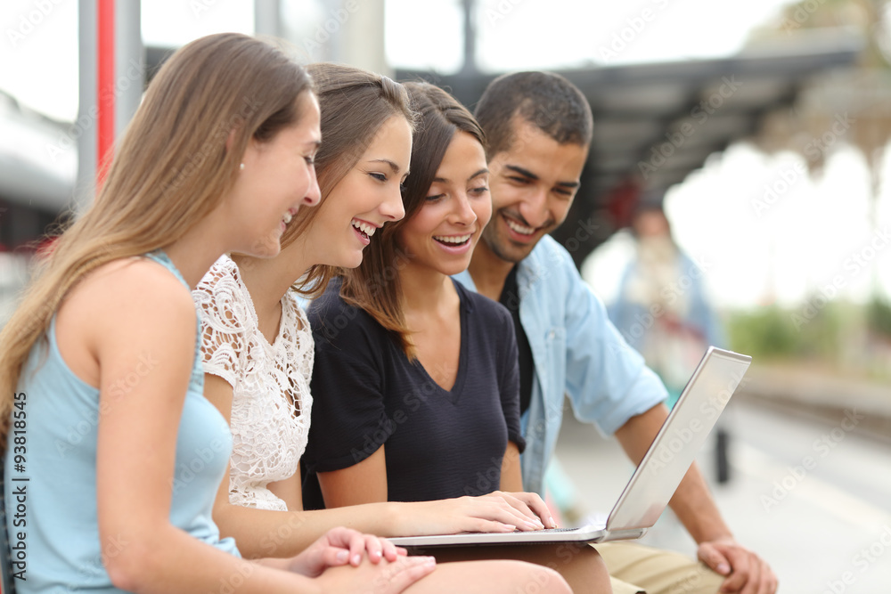 Four friends using a laptop in a train station Four friends using a laptop in a train station