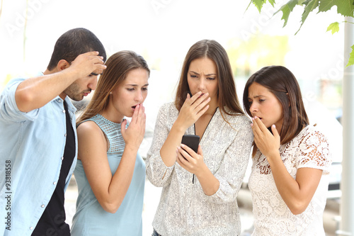 Four worried friends watching smart phone