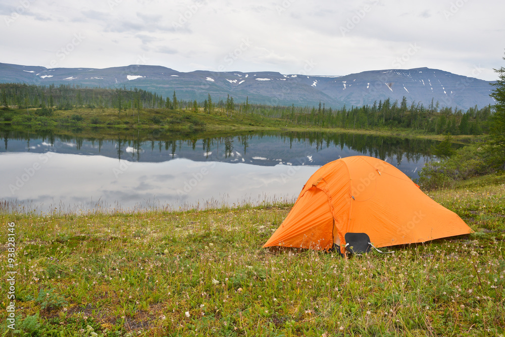 The tent on the lawn near the pond. Cloudy lake view, Putorana plateau, Taimyr, Russia.