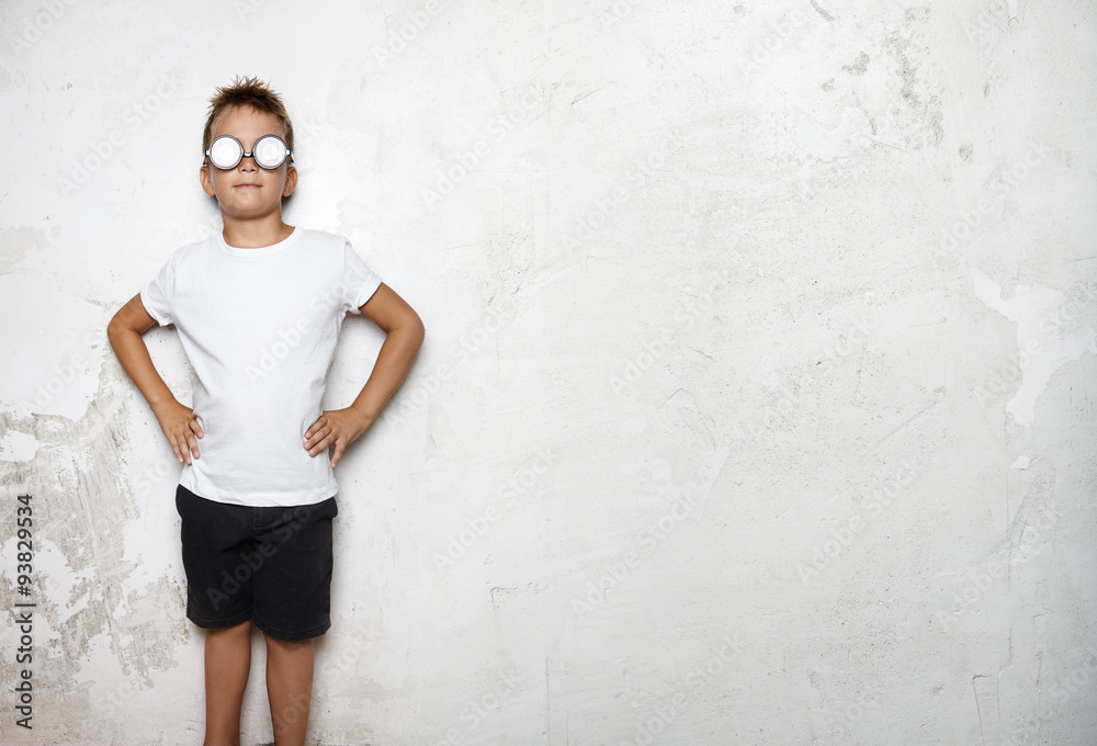Boy wearing white tshirt, shorts stands on a wall background of