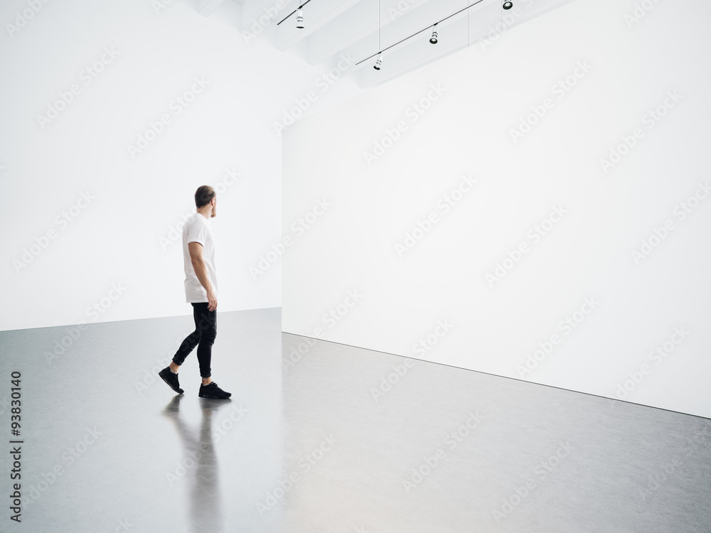 Young man walking in the empty, white gallery - obrazy, fototapety, plakaty 