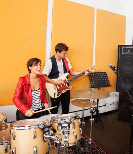 Female Drummer And Male Guitarist Performing In Studio