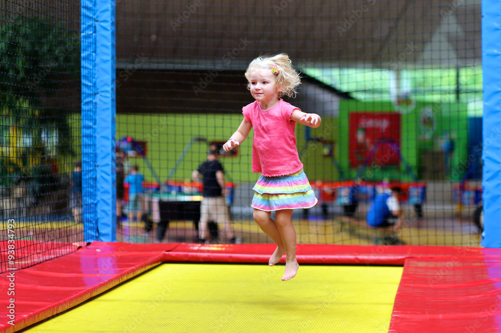 Little child jumping at trampoline in indoors playground. Active toddler girl having fun at sport centre.