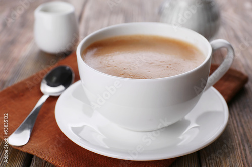 Cup of coffee with cream on brown napkin closeup