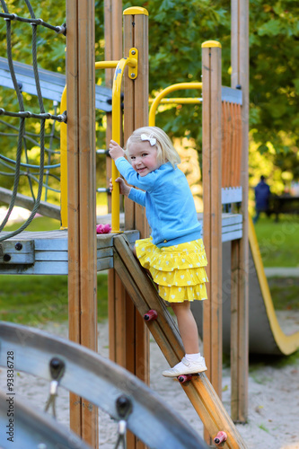 Happy kid enjoying activity in the park. Adorable little child, blond cute toddler girl, having fun outdoors climbing on playground on a sunny day