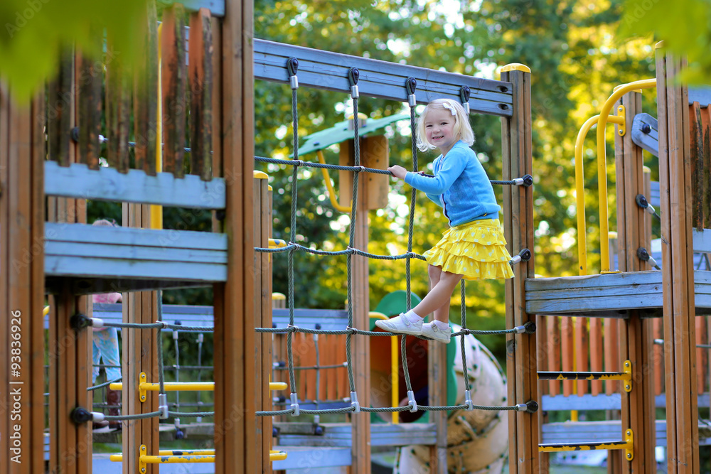 Happy kid enjoying activity in the park. Adorable little child, blond cute toddler girl, having fun outdoors climbing on playground on a sunny day