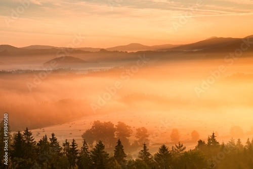 Fototapeta Naklejka Na Ścianę i Meble -  Pink daybreak in hilly landcape. Autumn freeze misty morning in a beautiful hills. Peaks of hills are sticking out from pink orange fog