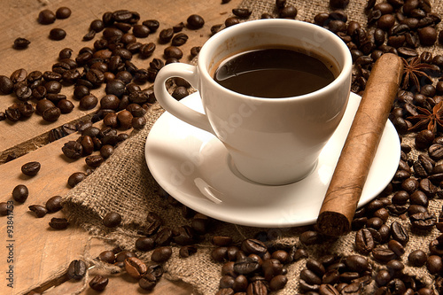 Coffee cup with coffee beans, cigar, cinnamon on bagging on wood.