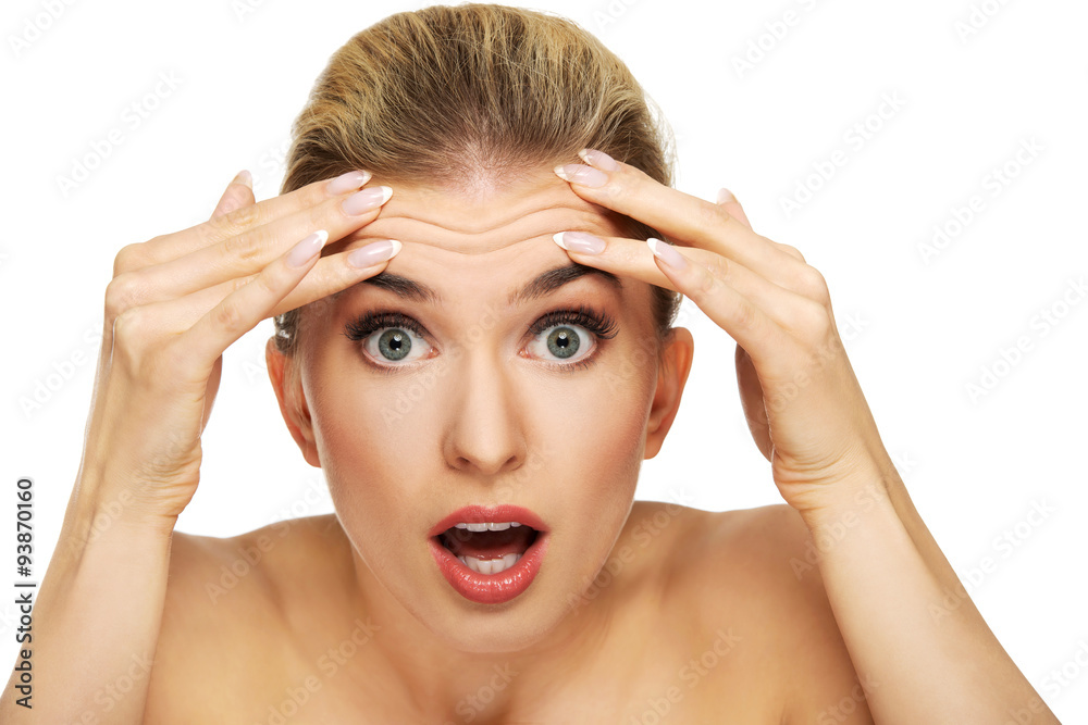 A young woman checking wrinkles on her forehead A young woman checking wrinkles on her forehead