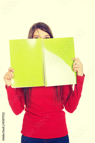 Woman hiding her face behind a notebook.