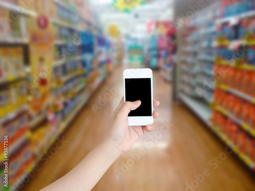 hand holding mobile phone with supermarket shelves aisle blurred