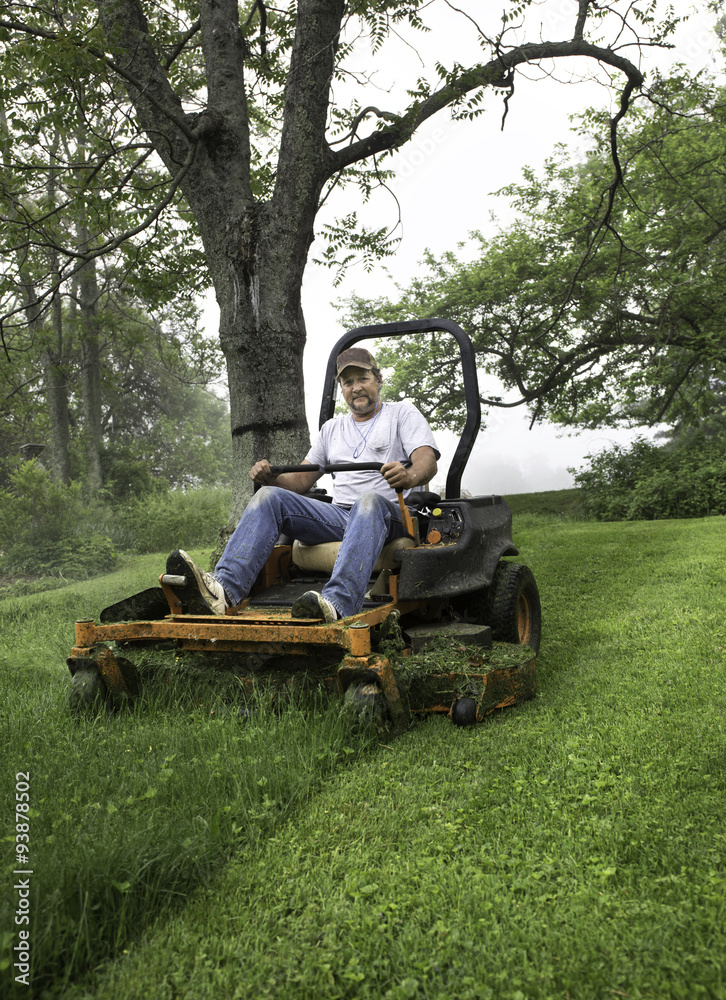 Man cutting grass on riding lawnmower in yard with trees Man cutting grass on riding lawnmower in yard with trees