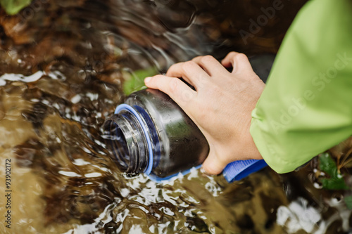 Принти на полотні woman taking water from forest spring on hiking trip