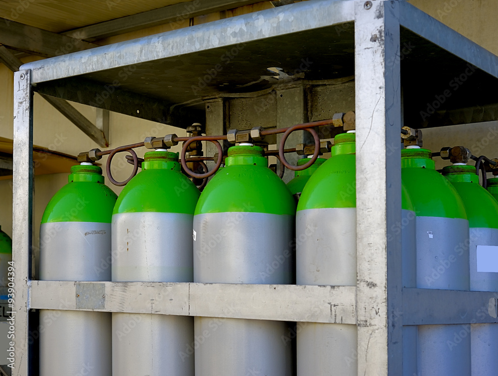 A group of industrial gas cylinders arranged in a rack on the outside of a factory A group of industrial gas cylinders arranged in a rack on the outside of a factory