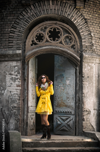 Full-length portrait of a pretty woman in yellow overcoat standing in front of a vintage door © rodjulian